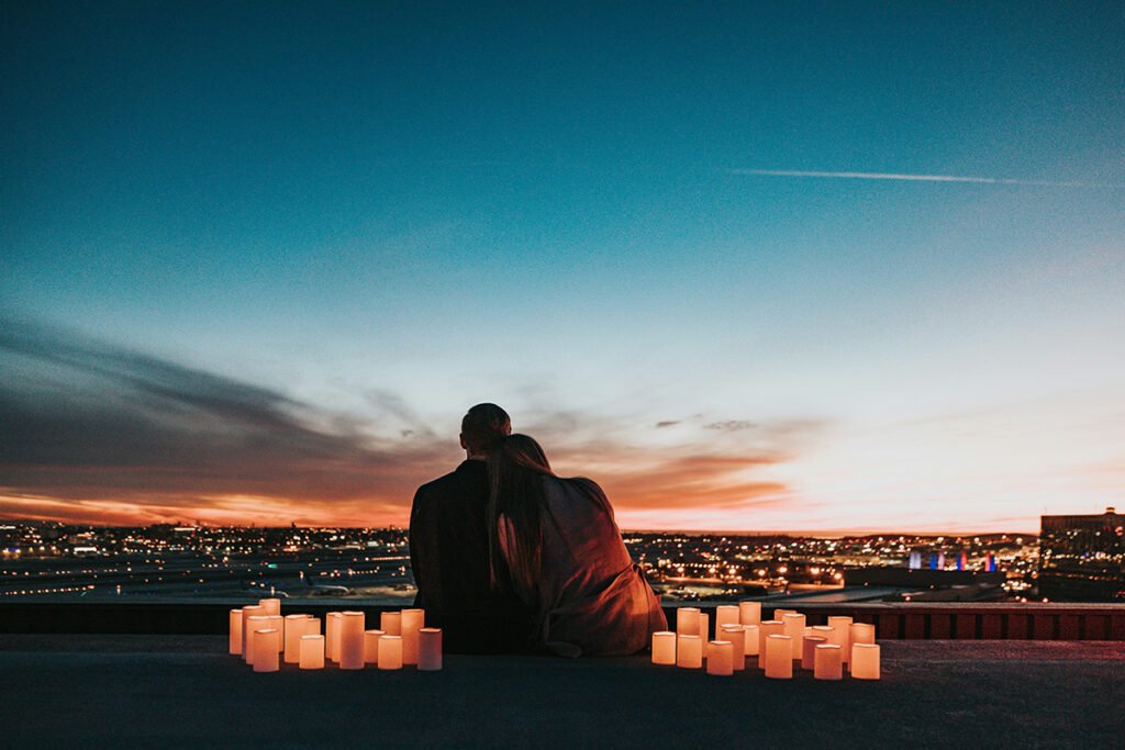 A couple surrounded by candles looking at a skyline sunset.